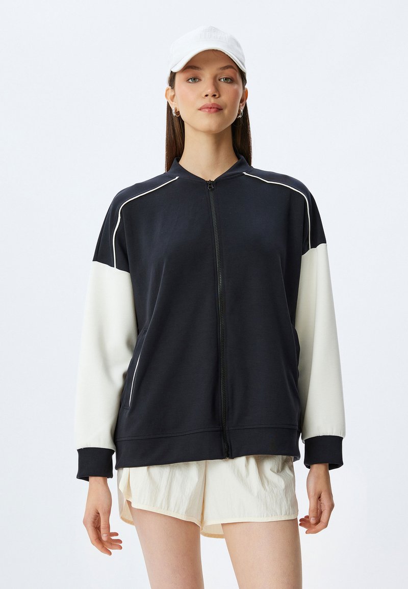 Svart och vit zip-up sweatshirt med hög krage, ribbade mudd och kontrasterande ärmdesign. Slät tyg med avslappnad passform.
