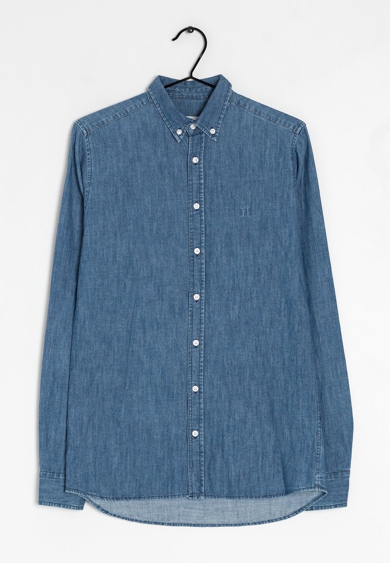 Camisa de mezclilla en azul medio, de mangas largas, con cuello botón, que presenta una tapeta delantera con botones blancos y un sutil logotipo en el pecho.