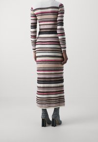 Lång, figurnära klänning med horisontella ränder i olika färger som inkluderar beige, svart och rosa. Texturen verkar mjuk; hög halsringning, långa ärmar.