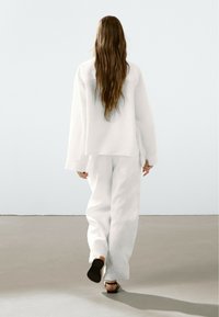 White linen oversized shirt and pants, featuring a relaxed fit and long sleeves. Simple design with a smooth texture, paired with black sandals.