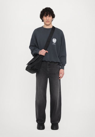 Szary sweatshirt z logo, czarne szerokie jeansy i czarna torebka na ramię. Model nosi czarne buty na platformie. Prosty, casualowy design.