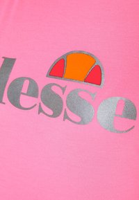 Camiseta de algodón rosa que presenta un gran logo gris con un diseño estilizado en naranja y rojo encima del nombre de la marca.