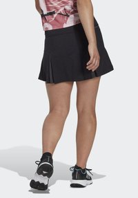 Juoda sportinė sijonas su priekiais, derinama su juodais ir baltais sportbačiais, kuriuose yra mėlynai žali akcentai. Lygus audinys, prigludusi juosmens juosta.