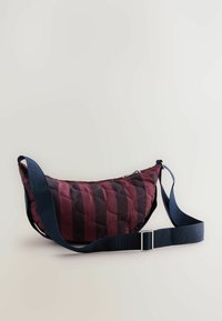Satelīts ar quilted dizainu, bordo un tumši zila krāsā, ar izliekta formu, regulējamu jostu un rāvējslēdzējs ar metāla vilkšanas tab.
