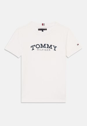 Balts īsām piedurknēm apakšvējums ar apaļu kakla izgriezumu, uz kura priekšpuses ir apdrukāts "TOMMY HILFIGER" tumši zils, un kreisajā piedurknē ir neliels zīmola karogs.