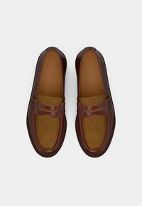 Par de sapatos de couro castanho tipo loafers com palmilha em camurça e detalhe de tira tipo penny, vistos de cima sobre um fundo branco.