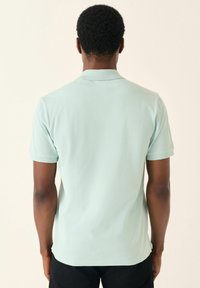 Polo de color verde menta claro fabricado en una tela suave, con un cuello clásico y mangas cortas, con una textura suave y sin patrones visibles.