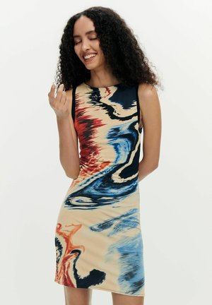 Frau mit lockigem Haar, die ein ärmelloses Kleid mit abstrakten rot-blauen, schwarzen und beigen Wirbelmustern trägt und mit geschlossenen Augen lächelt.