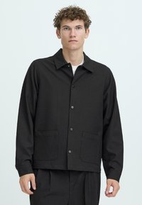 Black button-up jacket with a collar, two patch pockets, and a relaxed fit. Made of smooth fabric with a plain texture.