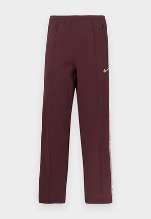 Calças de fato na cor borgonha com uma textura suave, bolsos laterais com fecho de correr e uma faixa branca com texto ao longo das costuras exteriores. Logótipo da Nike em dourado.