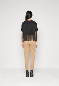 Černý crop top s třásněmi a kulatým výstřihem, v kombinaci s zúženými béžovými kalhotami a černými kotníkovými botami. Minimalistické pozadí.