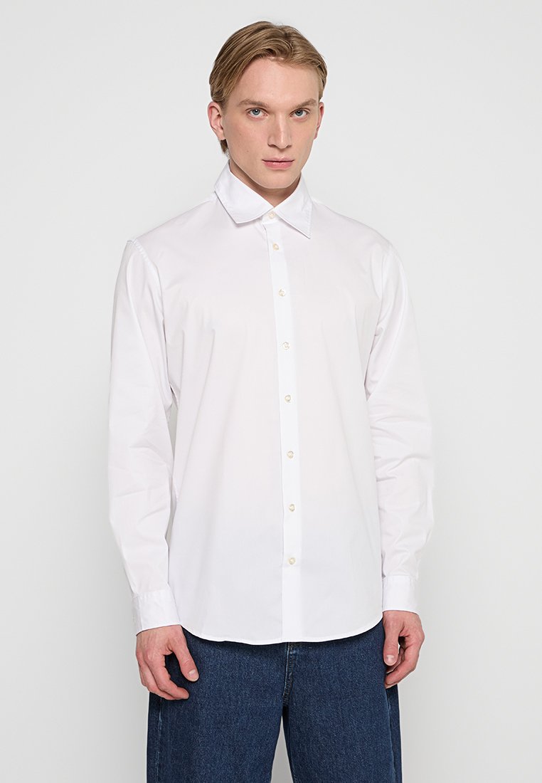 Camicia bianca a maniche lunghe realizzata in tessuto liscio, con colletto classico e chiusura frontale con bottoni di colore chiaro.