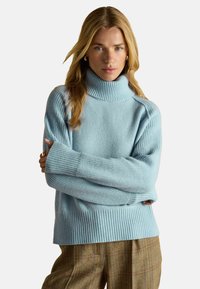 Pulover bleu deschis cu guler înalt, dintr-un tricot moale și texturat, cu detalii ribbatate la manșete și la tiv. Croială lungă, lejeră, cu umeri căzuți.