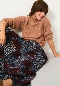 Strickpullover in hellem Pfirsich mit Zopfmuster; langer gemusterter Rock in Marineblau, Burgunderrot und Weiß; weiche Textur; geschichtetes Design mit unterschiedlichen Druckmotiven.