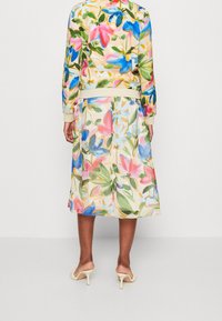 Blomstret jakke og nederdel i pastelfarver, prydet med blå og pink blomster på en lys creme baggrund, med en tætsiddende talje og blød tekstur.