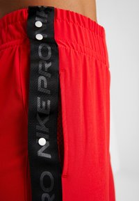 Pantalones cortos deportivos rojos con una cintura negra con la marca Nike, que cuentan con botones de presión y bolsillos laterales. El material es ligero con una textura suave.