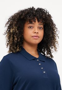 Polo shirt blu navy con colletto, caratterizzato da una pattina con bottoni e dettaglio del logo ricamato. Maniche corte e tessuto testurizzato.