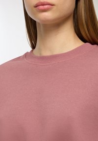 Felpa rosa con colletto a coste, tessuto morbido e superficie liscia, che mostra una vista ravvicinata della parte superiore del torace.