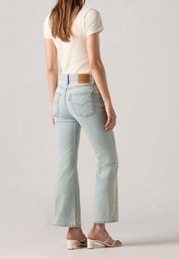 Jeans de mezclilla de corte acampanado y color azul claro con una cintura alta y bolsillos traseros. Combinados con una camiseta blanca de canalé y tacones blancos.