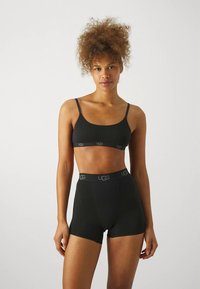 Svart sømløs bralette med tynne stropper og logo-bånd. Matchende høyt liv svarte boyshorts med logo-bånd. Glatt tekstur.