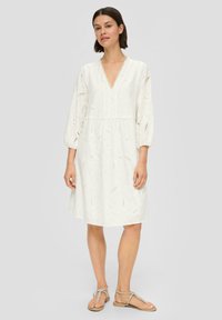 Robe blanche en coton avec un décolleté en V, des manches ballon et des détails en dentelle. Présente une jupe fluide et un motif paisley complexe.