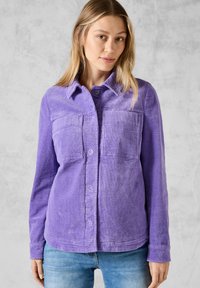 Aidot corduroy-pusero purppuran värinen, napitettavalla edellä, kahdella rintataskulla ja kauluksella, joka on tekstiililtään teksturoitu ja pitkähihainen.