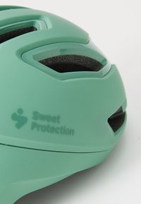 Casque vert menthe avec des fentes de ventilation, intérieur texturé noir et logo en relief. Surface lisse avec un design moderne.