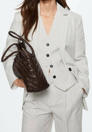 Borsa in pelle marrone intrecciata con forma arrotondata e manici intrecciati coordinati, abbinata a un completo a righe chiare con giacca aderente.