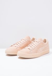 Ljusrosa mockaskor med platta snören, en texturerad gummisula och sidologga. Klassisk låg topp design med perforerade detaljer.