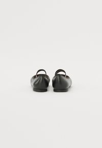 Svarta läderballerinas med rund tå, som har en liten klack och ett band bak med varumärkesdetalj. Slät yta.