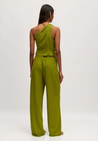 Groen twee-delig outfit met een top met één schouder en losvallende broeken met een elastische tailleband, gemaakt van zachte stof.