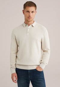 Krēmskrāsas polo sporta krekls ar teksturētu rakstu, pogāta henley apkakle un ribots aproces. Stilizēts ar tumšām džinsām.