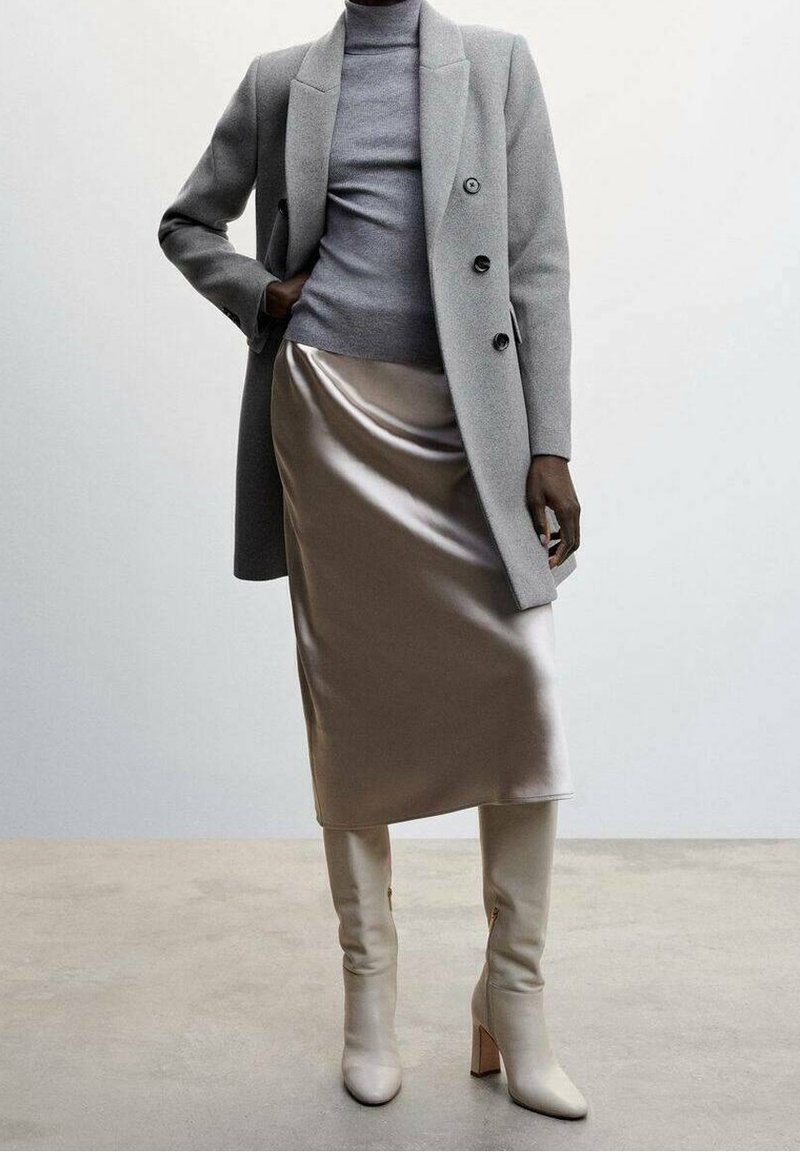 Grå uldfrakke med store knapper, tætsiddende grå turtleneck, satin beige nederdel og knæhøje cremede støvler med blokhæle. Glatte teksturer.