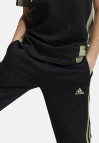 Pantalones deportivos negros y una camiseta negra-verde, fabricada en algodón, con bolsillos laterales y un logo verde bordado en los pantalones.