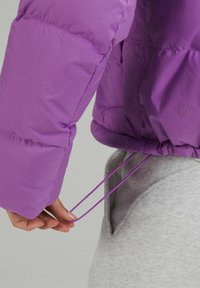 Doudoune violet vif avec ourlet resserré, dotée de cordons élastiques et d'une finition texturée. La doublure intérieure est grise et lisse.