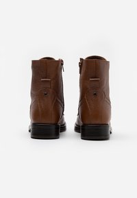 Brązowe skórzane botki za kostkę z teksturowanym wykończeniem, czarną gumową podeszwą oraz bocznymi zamkami błyskawicznymi dla łatwego zakładania. Minimalistyczny design z okrągłym noskiem.