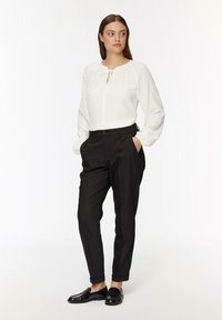 Blouse blanche texturée avec un décolleté en trou de serrure et un col à nouer, manches longues, associée à un pantalon noir ajusté et des mocassins noirs. Design simple et épuré.