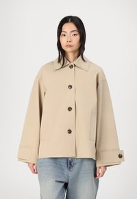 Beige croppet jakke med stor krage, knappelukking og klaffelommer. Har vide ermer med knappedetaljer og myk tekstur.