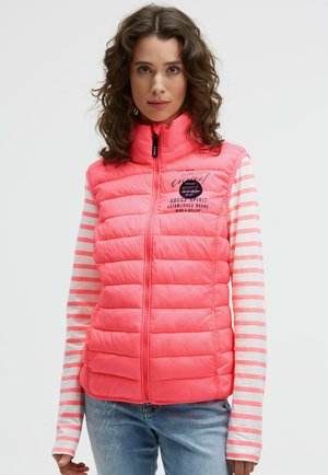 Rosa Pufferweste mit hohem Kragen und Reißverschluss. Verfügt über ein gestepptes Design und ein Logo auf der Brust. Getragen über einem gestreiften Langarmshirt.