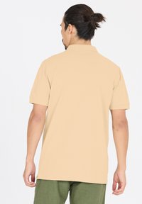 Beige polo paita lyhyillä hihoilla, yksinkertainen muotoilu ja kaulus. Kevyt kangas, jossa on sileä rakenne, yhdistettynä vihreisiin housuihin.