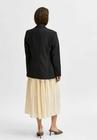 Černý blazer se strukturovanými ramenními vycpávkami, doplněný volnou smetanovou sukni. Sukně má vícevrstvý design a plisé texturu.