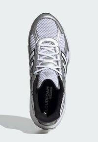 Biele športové topánky z priedušnej sieťoviny s striebornými akcentmi a čiernymi detailmi. Obsahujú okrúhle šnúrky, logo na jazyku a značenie "CLOUDFOAM COMFORT" vo vnútri.