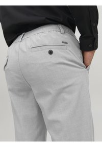 Pantaloni grigi chiari realizzati con un tessuto strutturato, cintura elastica, tasca posteriore con bottone e un dettagli logo discreto.