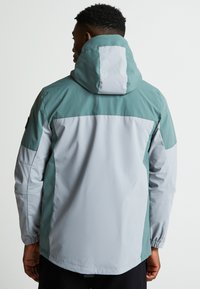 Veekindel jakk helesinise ja heledashalli värviga. Omab kapuutsi, elastseid mansette ning värvide segamise disaini koos siledaga kangatekstuuriga.