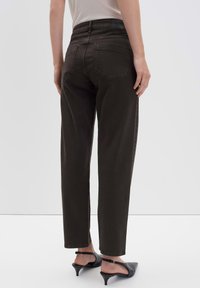 Donkerbruine high-waisted jeans met een rechte pijp, achterzakken en subtiele stiksels, gecombineerd met zwarte hoge haksandalen.