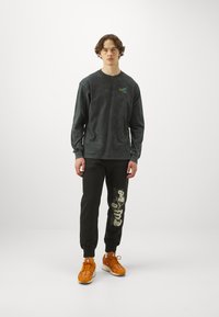 Dark gray long-sleeve shirt with logo, paired with black joggers featuring a graphic print. Orange sneakers complete the outfit.