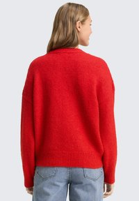 Czerwony sweter z dzianiny o luźnym kroju, z okrągłym dekoltem i prążkowanym wykończeniem na dole. Wykonany z teksturowanego materiału, z opuszczanymi ramionami i długimi rękawami.