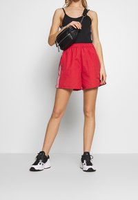Red shorts with a textured finish, elastic waistband, and white side stripes. Black athletic sneakers with a chunky sole and laces.