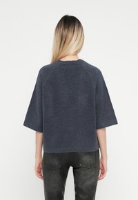 Mörkgrå, kortärmad topp med rund halsringning, tillverkad av mjukt material med en slät textur, kombinerad med mörka, texturerade byxor.