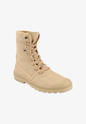 Botte beige en toile montante avec semelle en caoutchouc, lacets à l'avant, œillets métalliques et bout texturé, inclinée pour montrer le côté extérieur et l'avant.